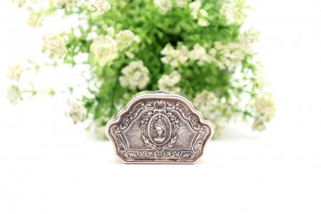 Caixa de comprimidos em prata com cena idílica e elementos vegetalistas relevado